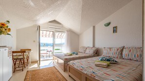 Ein Schlafzimmer mit zwei Betten, einem kleinen Tisch, einem Stuhl und Blick ins Freie.