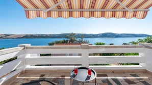Eine Terrasse mit Blick auf einen See und Berge, ein Tisch mit zwei Gläsern und ein gestreifter Sonnenschirm.
