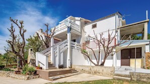 Ein modernes, zweistöckiges Haus mit weißer Fassade, einem Balkon und einem kleinen Garten mit Blumentöpfen.
