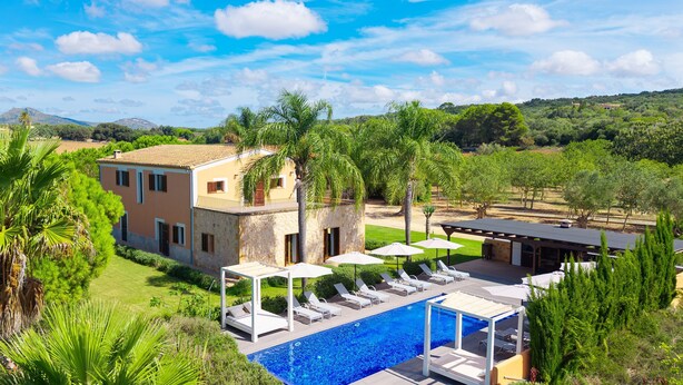 A villa with a swimming pool, outdoor seating, and a view of the surrounding landscape.