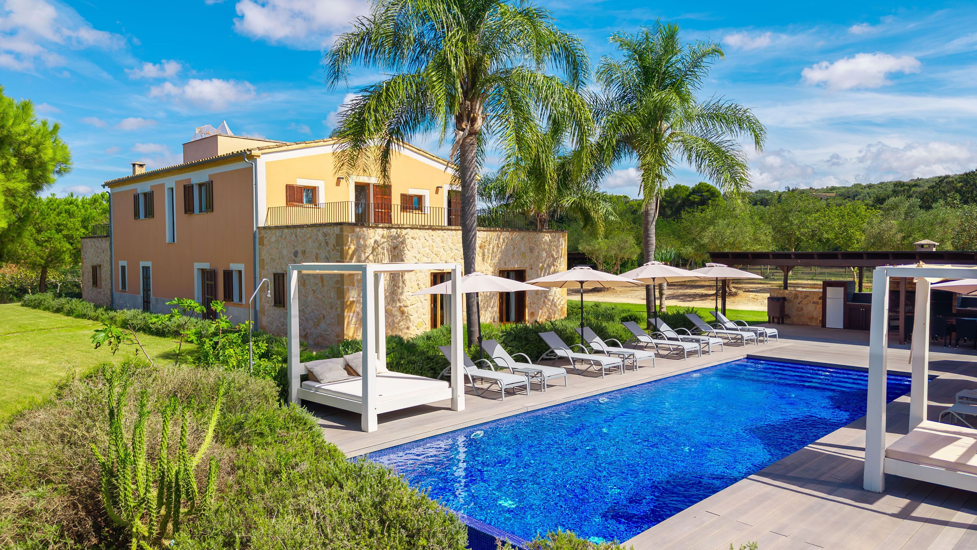 A poolside area with lounge chairs, a pool, and a building with stone walls and a balcony.