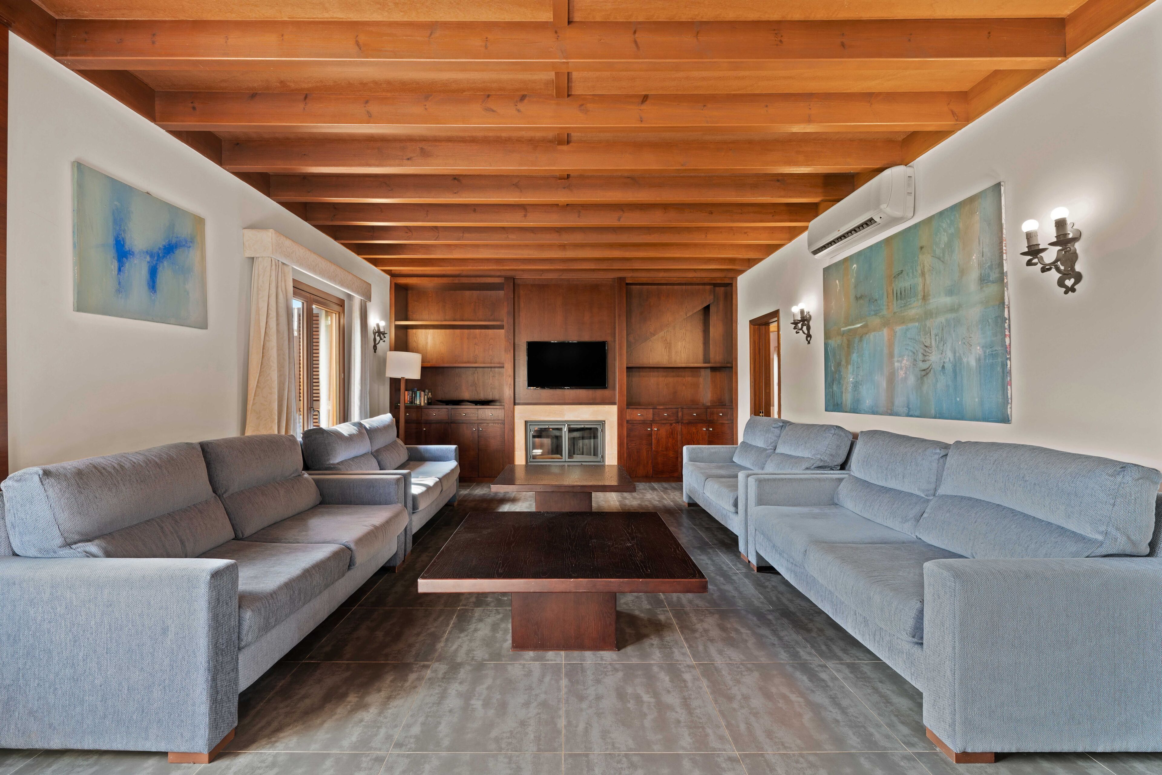 A modern living room with two grey sofas, a wooden coffee table, and a flat-screen TV mounted on the wall.