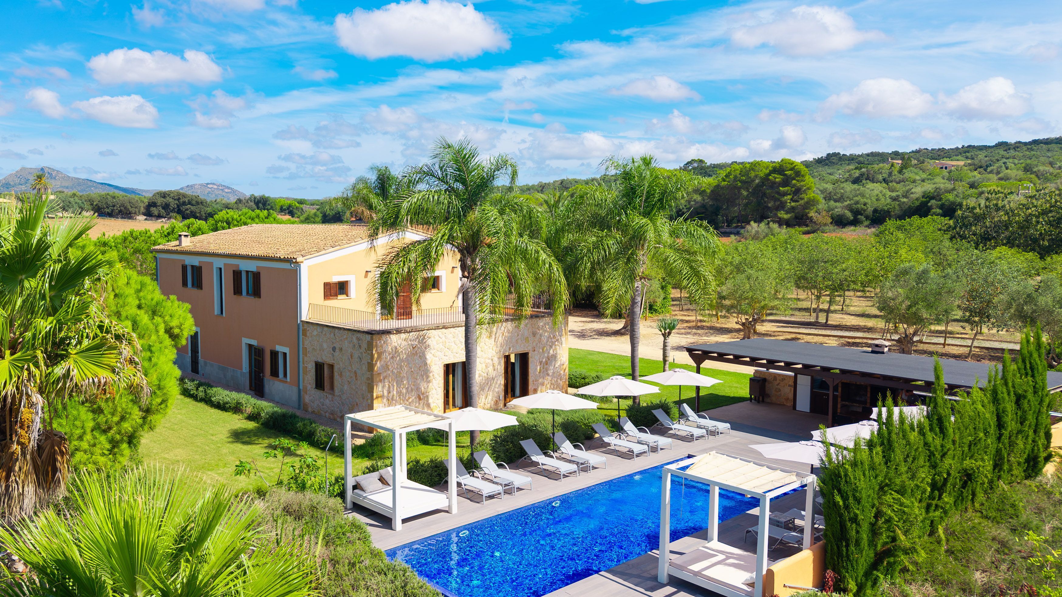 A villa with a swimming pool, outdoor seating, and a view of the surrounding landscape.