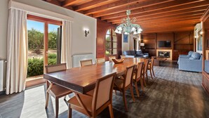 A spacious dining area with a wooden table and chairs, a chandelier, and a view of the outdoors.