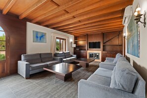 A spacious living area with a wooden ceiling, grey sofas, a fireplace, and a television.