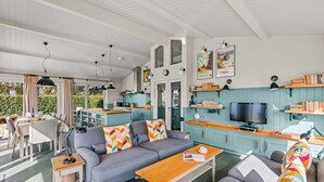 Un salon moderne avec un canapé gris, une table basse en bois et un téléviseur. On y trouve également un coin cuisine avec des meubles de couleur turquoise et un coin repas avec une table et des chaises.