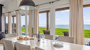 Un coin repas avec une table dressée pour deux personnes, offrant une vue sur un paysage verdoyant et la mer.