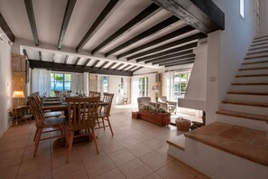 A spacious dining area with a wooden table and chairs, a large window with curtains, and a staircase leading to an upper level.