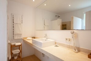 A modern bathroom with a large mirror, a sink, a towel rack, and a hairdryer.