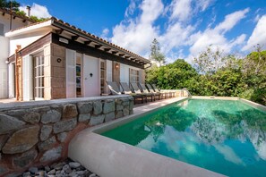 Ein Poolbereich mit Steinmauer, Liegestühlen und einem klaren, blauen Pool.