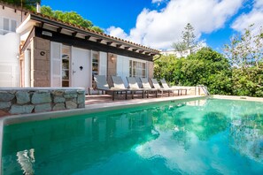 A pool area with lounge chairs and a stone wall.