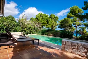 A poolside area with a lounge chair and a stone wall.