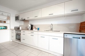 A modern kitchen with white cabinets, a built-in microwave, a coffee maker, and a dishwasher.