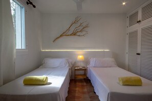 A room with two beds, a wall-mounted branch decoration, a nightstand with a lamp, and a window.