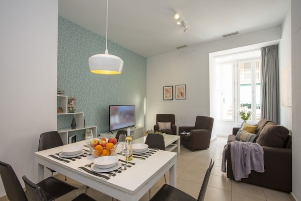 A modern living room with a dining area, a television, and a sofa.