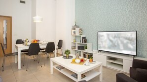 A modern living room with a white dining table, black chairs, a flat-screen TV, and a bookshelf. - Singular Stays Mar44 VII (Valencia)