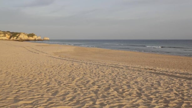 Una platja sorrenca amb petjades que condueixen a l'aigua i un penya-segada rocosa al fons.