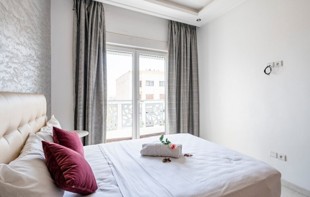 Camera d'albergo con un letto grande, tende grigie, una testiera bianca e vista sugli edifici esterni.