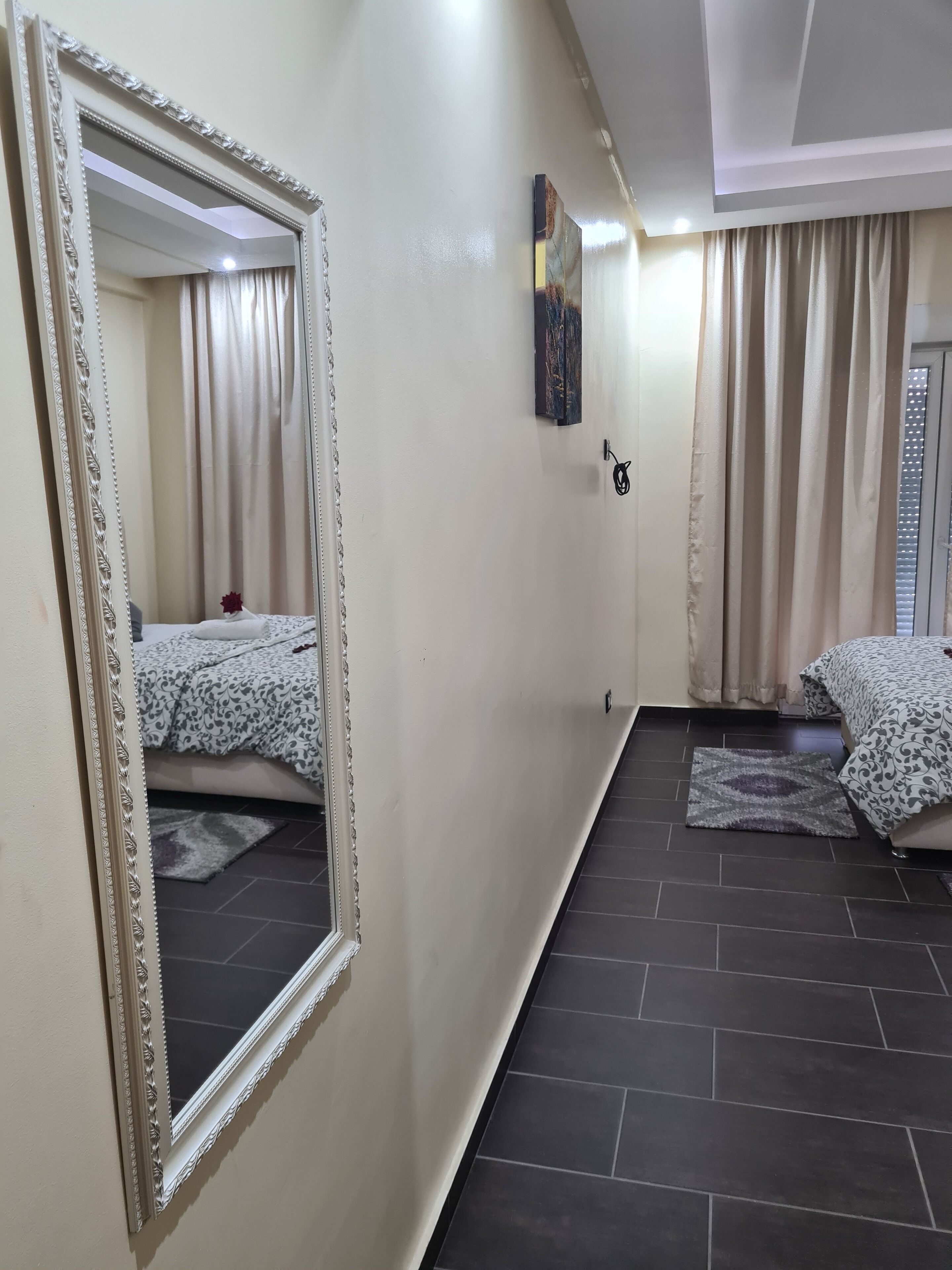 A bedroom with a large mirror, two beds with patterned bedding, a rug, and a painting on the wall.