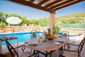 A covered outdoor dining area with a pool and a view of a hilly landscape.