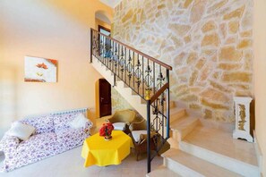 Un escalier avec un mur en pierre, une rampe en bois et une table jaune sur laquelle est posé un vase.