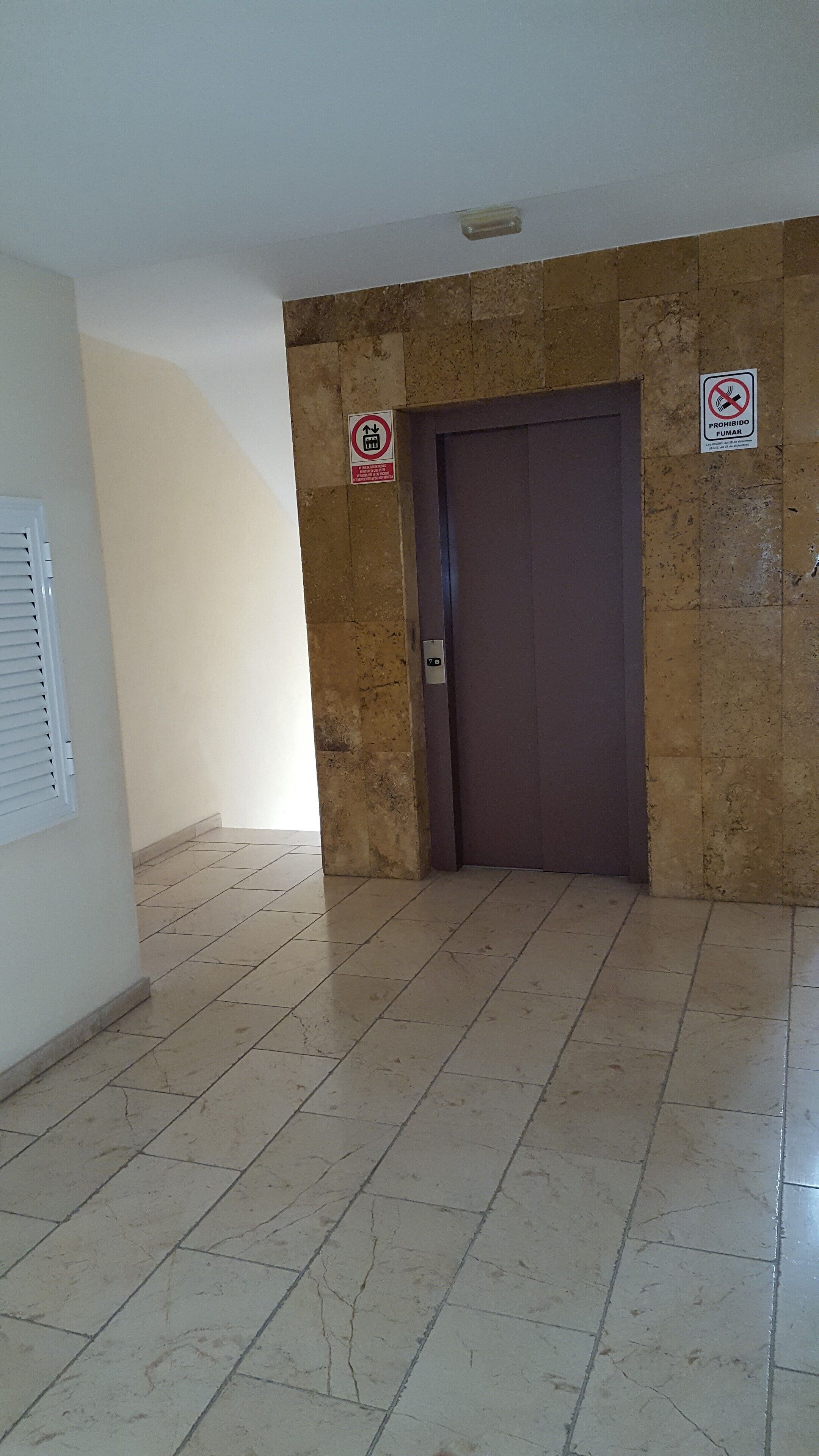 A hallway with a marble-tiled floor, a closed door, and two signs on the wall.