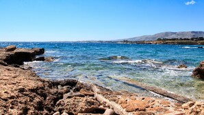 Eine felsige Küstenlinie mit klarem, blauem Wasser und Bergen in der Ferne.