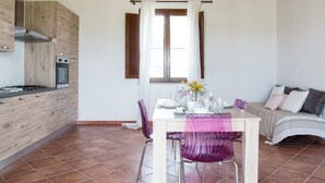 Eine moderne Küche mit Gasherd, Backofen und integriertem Dunstabzug. Ein Esstisch mit Stühlen und ein Fenster mit Vorhängen.