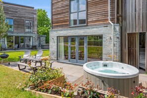 Ein modernes Haus mit Natursteinfassade, einer Terrasse mit Gartenmöbeln und einem Whirlpool.