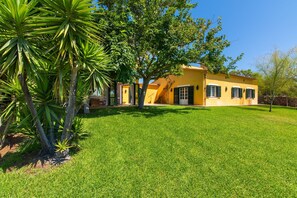 A yellow house with a well-maintained lawn and a large tree in the foreground.
