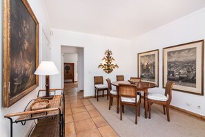 A dining area with a round table, six chairs, a lamp, and two framed pictures on the wall.