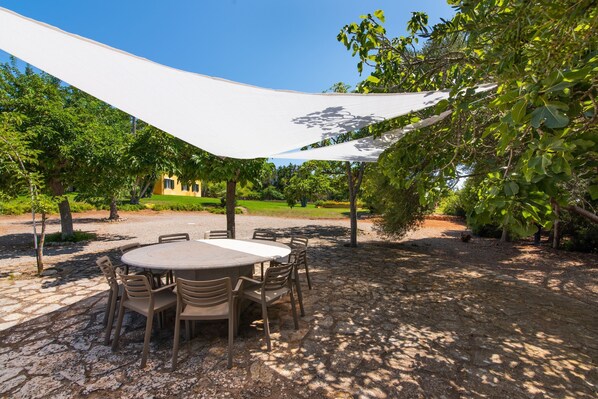 An outdoor patio with a round table and chairs, surrounded by trees and a white canopy.