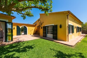 A yellow building with a tiled patio, green shutters, and a well-maintained lawn.