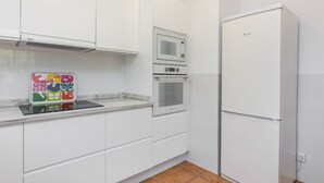 Een keuken met witte kasten, een magnetron, een oven en een koelkast.