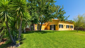 Een geel huis met een verzorgd gazon en een grote boom op de voorgrond.