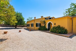 A yellow building with a gravel driveway and potted plants.