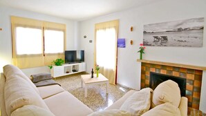 Una sala de estar con un sofá, un televisor, una mesita y una chimenea.