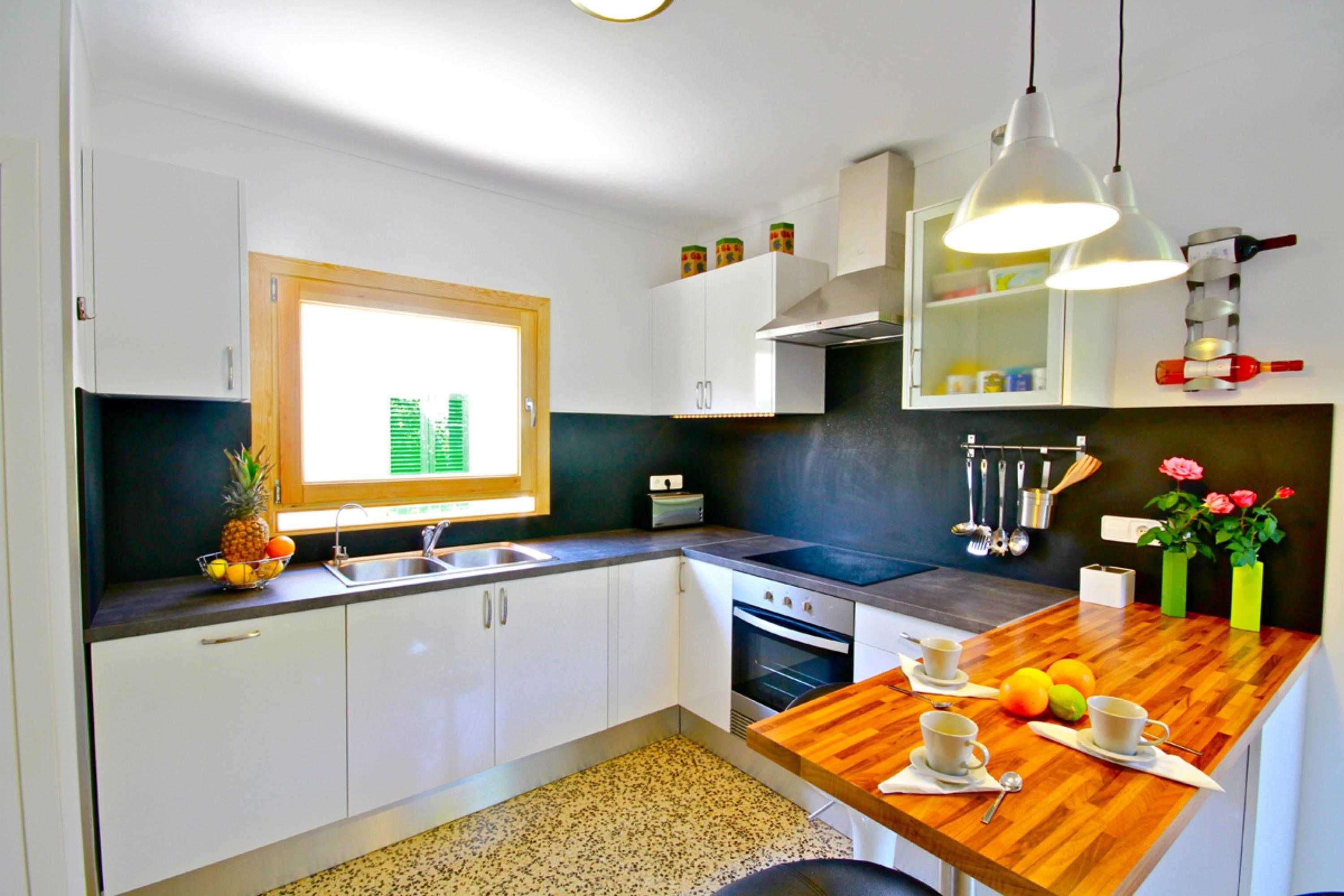 A modern kitchen with white cabinets, a wooden countertop, a built-in oven, and a window with blinds.