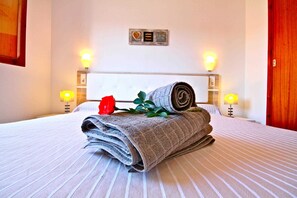 A neatly made bed with rolled towels and a red rose, two wall-mounted lamps, and a plaque on the wall.
