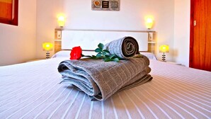 Una cama bien hecha con toallas enrolladas y una rosa roja, dos lámparas de pared y una placa en la pared.