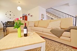 Un salon comprenant un canapé, une table basse, une horloge, un escalier et un coin repas.