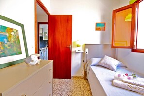 Un dormitorio con cama, cómoda, puerta roja y un cuadro en la pared.