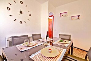 Comedor con un reloj, una mesa lista para dos personas y una puerta roja al fondo.