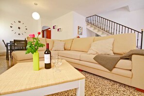 Una sala de estar con sofá, mesa de centro, reloj, escalera y comedor.