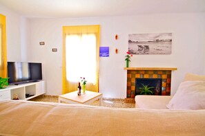 Una sala de estar con televisión de pantalla plana, chimenea, sofá, mesa de centro y un cuadro en la pared.