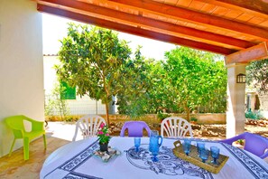 An outdoor patio with a table set for dining, surrounded by chairs and a pergola overhead.