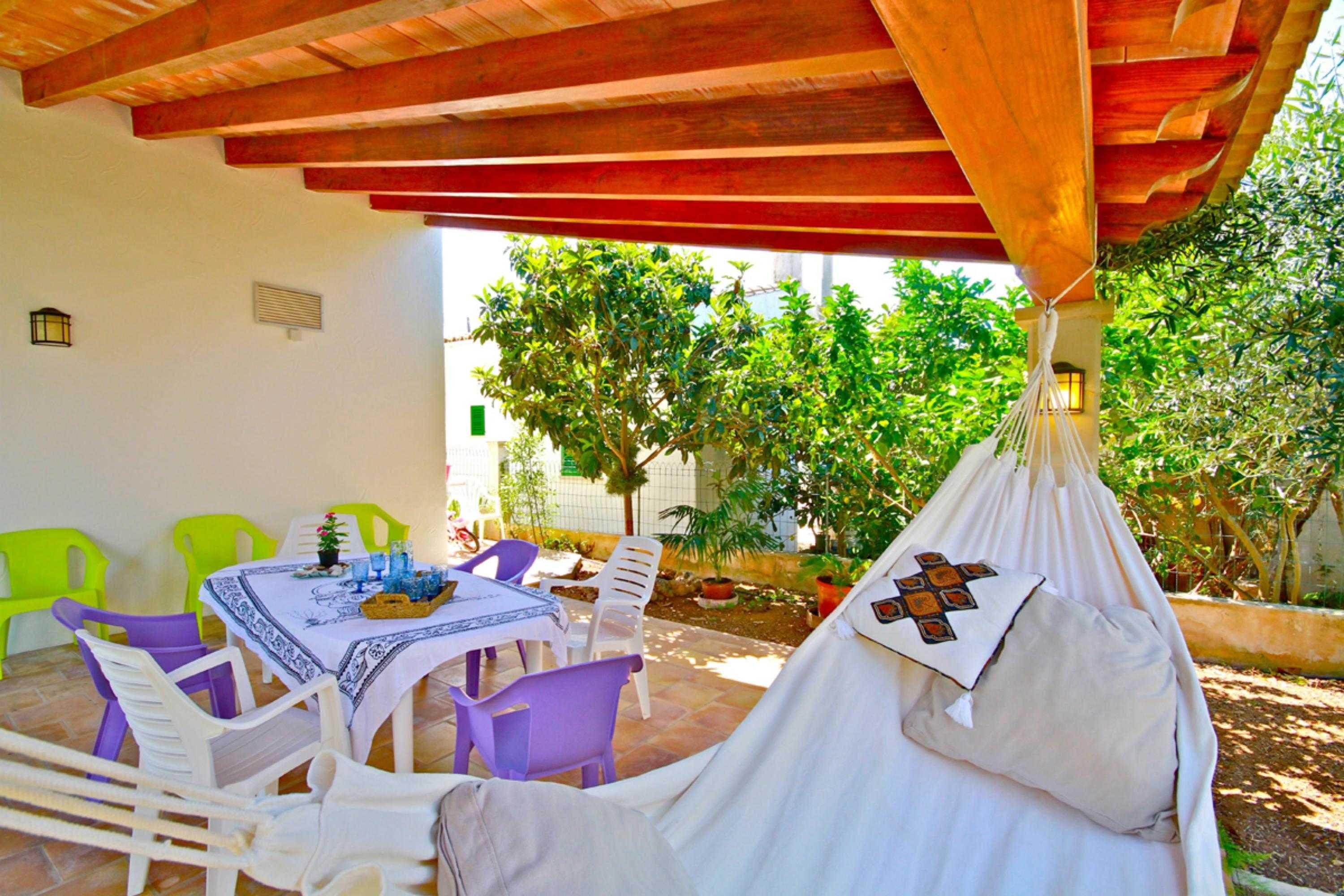A covered outdoor seating area with a table, chairs, and a hanging hammock.