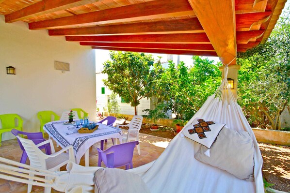 A covered outdoor seating area with a table, chairs, and a hanging hammock.