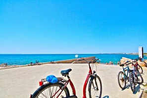 Una zona costera con bicicletas estacionadas junto al mar, un paseo marítimo de hormigón y un cielo azul despejado.