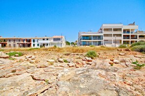A coastal building with multiple balconies, a flat roof, and a rocky foreground.